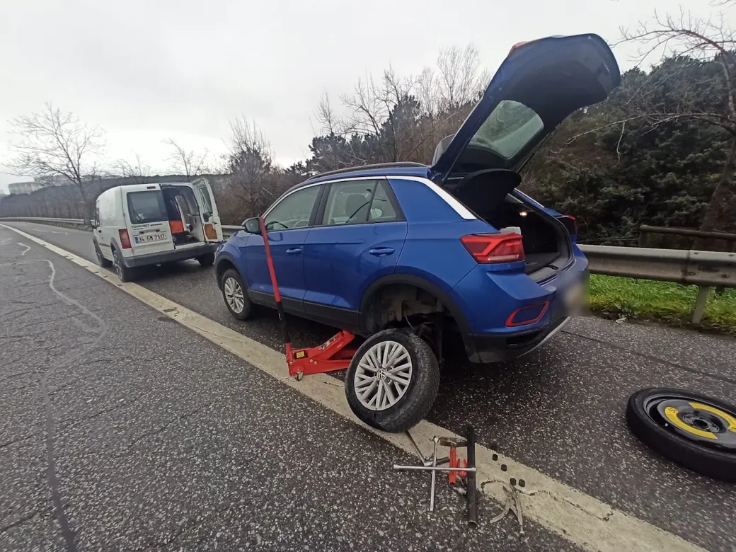Otoyol kenarında krikoya alınmış araçta stepne değişimi, arkada kapıları açık servis aracı